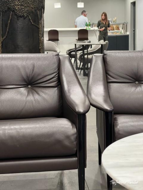 Dark brown leather lounge chairs at Piranesi Lounge Milan Linate, with the bar area visible behind