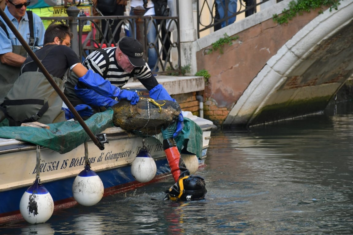 Diver and crew retrieving a submerged bronze statue from a Venice canal beside a small boat