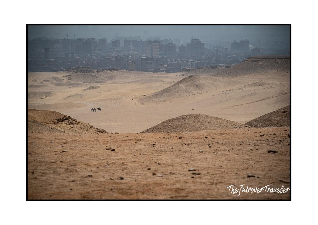 Two horse riders crossing the Giza desert plateau with hazy Cairo skyline in the background