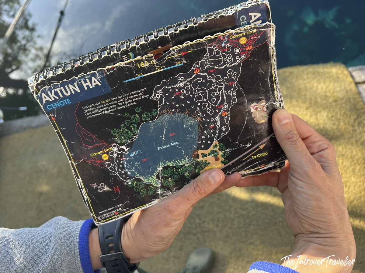 Dive guide holding a detailed underwater map of Aktun Ha cenote, showing cavern limits and snorkel areas