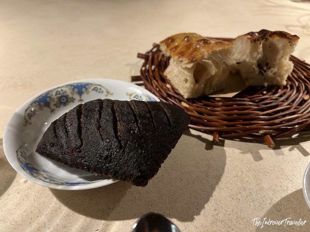 Dark squid ink bread roll and focaccia served as starters at Trattoria Da Lucio, Rimini