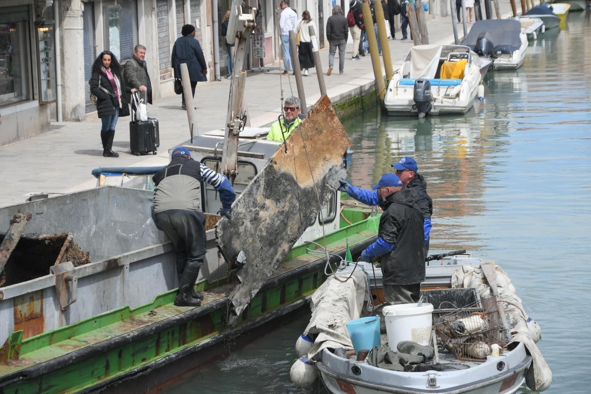 Workers on boats in a Venice canal hauling large debris slabs during a canal cleanup operation