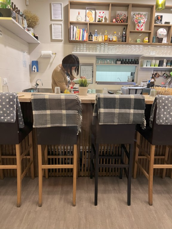Interior of Yuzuya Japanese restaurant in Bologna, with bar stools and a lucky cat on the shelf