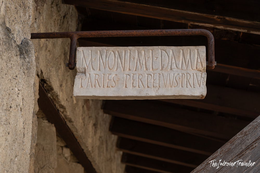 Ancient Roman Latin inscription on a marble tablet hung on a rusted bracket at Herculaneum excavations