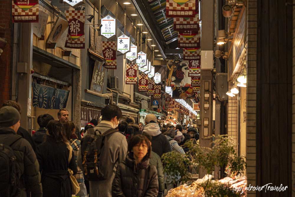 Crowded indoor arcade of Nishiki Market in Kyoto, lined with red and white shop banners