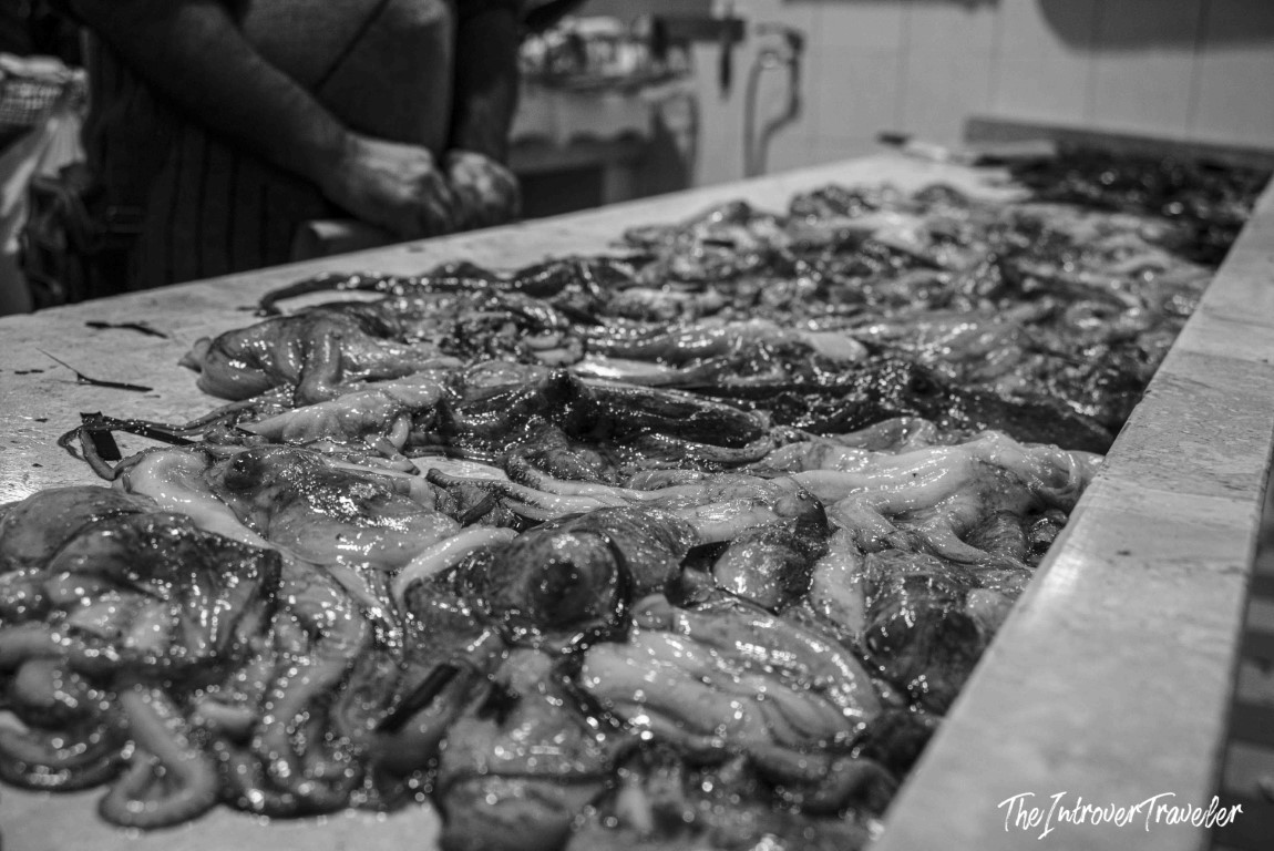 Fresh squid and octopus spread across a marble counter at a bustling coastal fish market