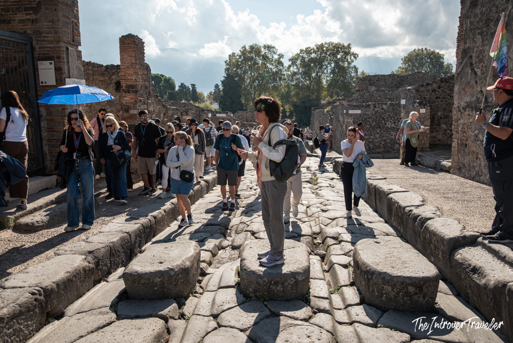 Crowds of tourists walking on ancient Roman stepping stones across a cobbled street in Pompeii