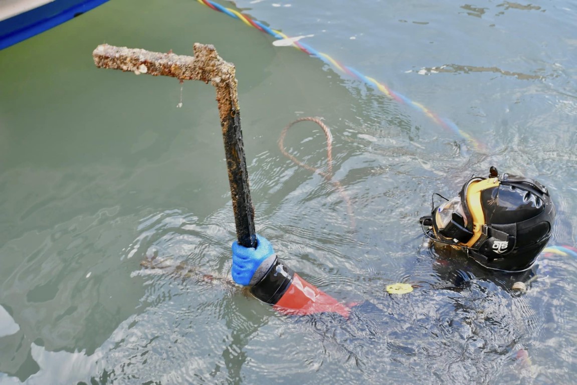 Diver surfacing in a Venice canal holding a barnacle-encrusted metal object recovered from the water