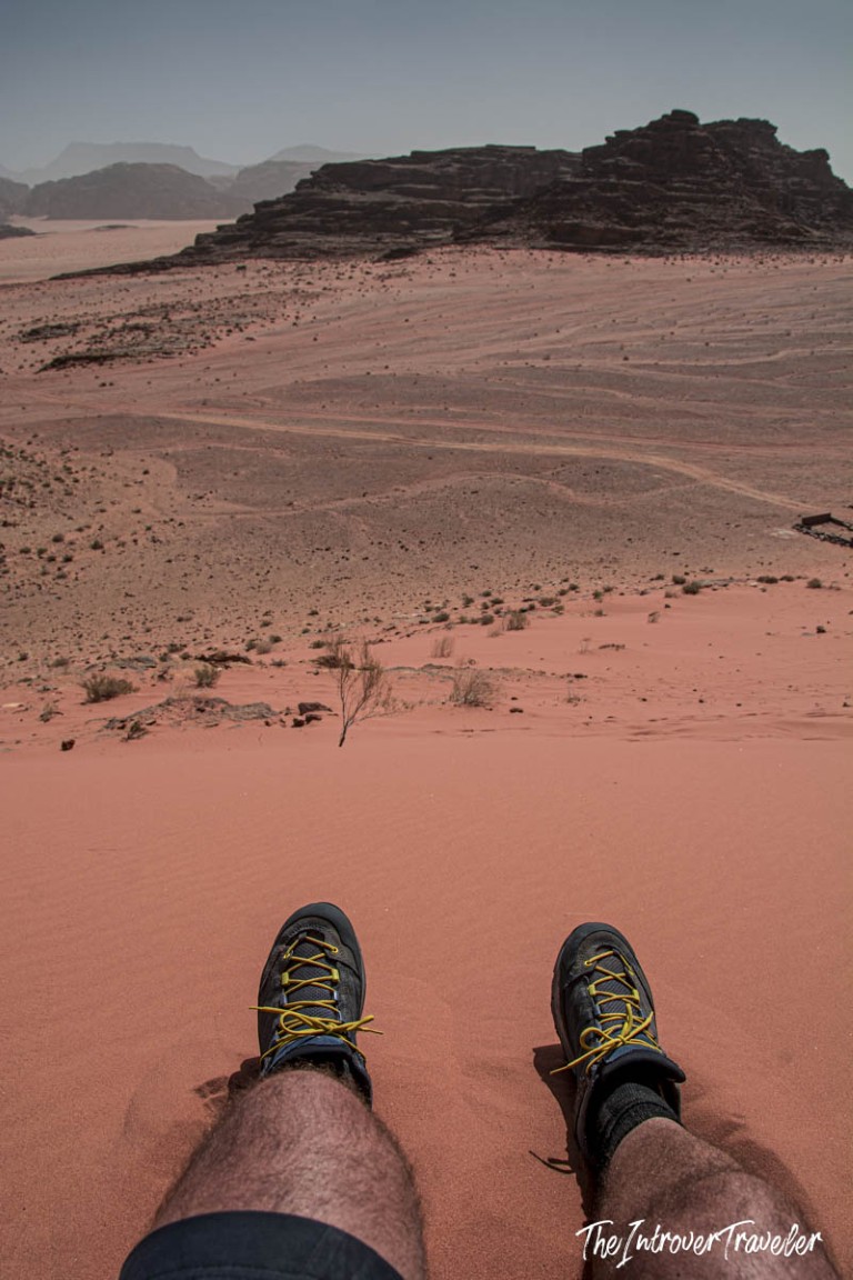 Hiker resting on a red sand dune in Wadi Rum desert, Jordan, with rocky mountains in the background