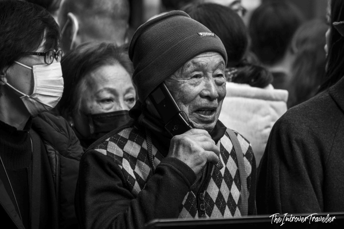 Elderly Japanese man on phone amid the busy crowd at Tsukiji fish market, Tokyo