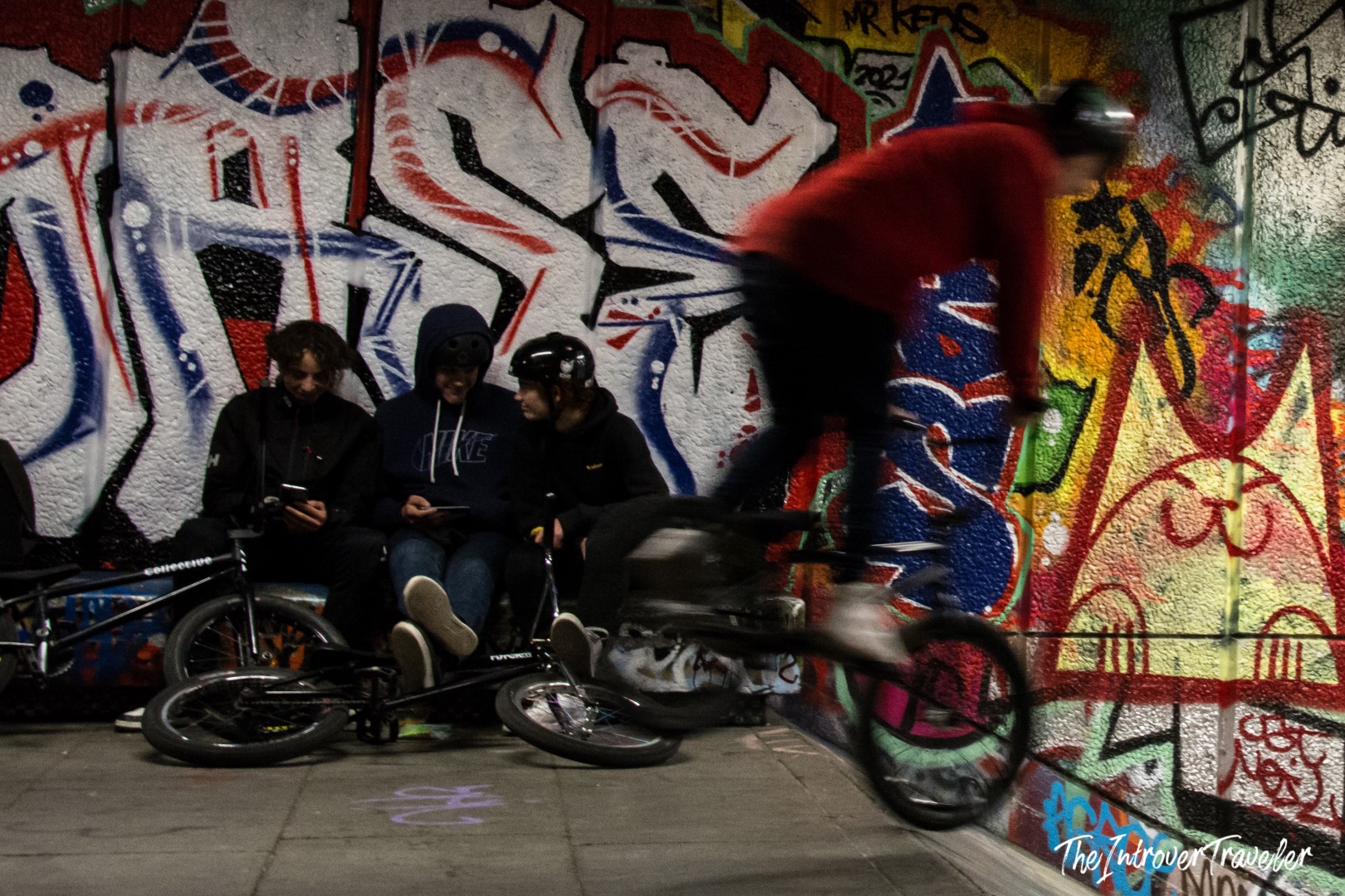 BMX riders at the Southbank skate spot, with vivid graffiti murals covering the walls behind them