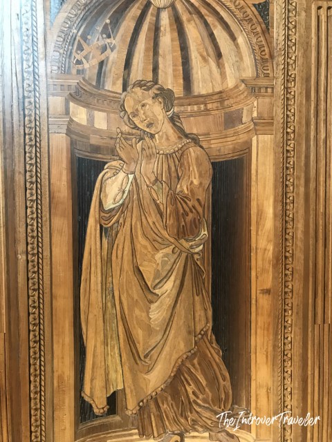 Detailed wood intarsia panel in the Studiolo of Federico da Montefeltro, Urbino, depicting a robed female figure under a classical dome.