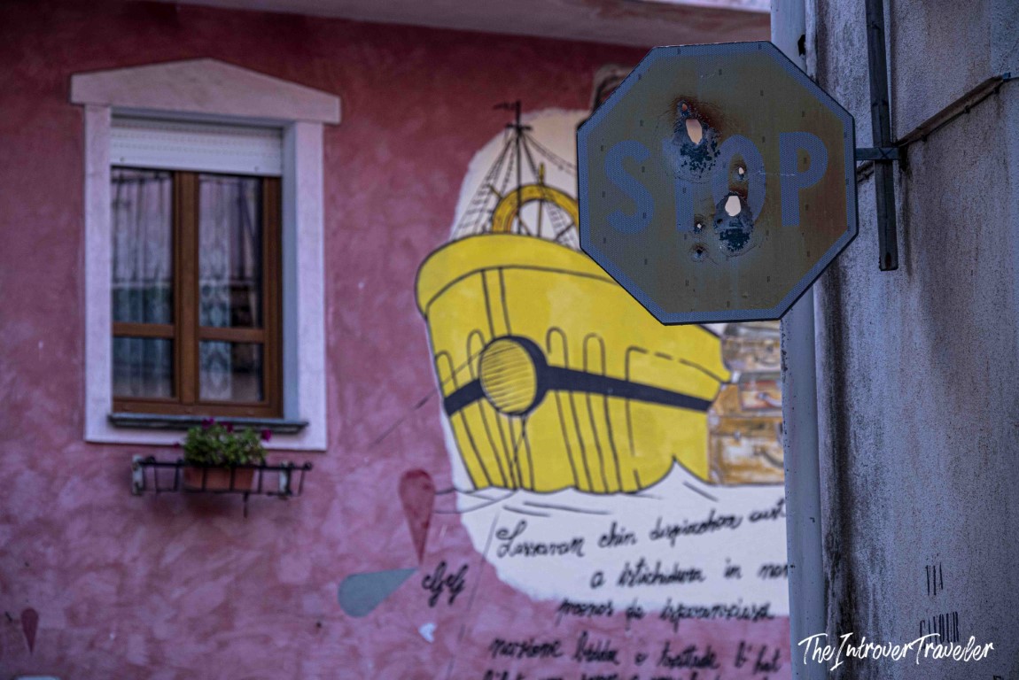 Bullet-riddled stop sign in front of an Orgosolo mural depicting a yellow ship, Sardinia