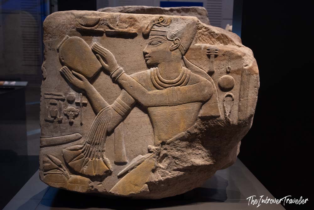 Ancient Egyptian limestone relief fragment showing a figure making an offering, on display at the Grand Egyptian Museum in Cairo