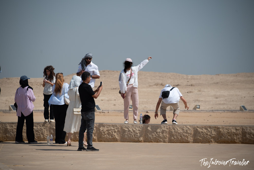 Tourists taking photos and posing on a stone wall at the Pyramids of Giza desert plateau