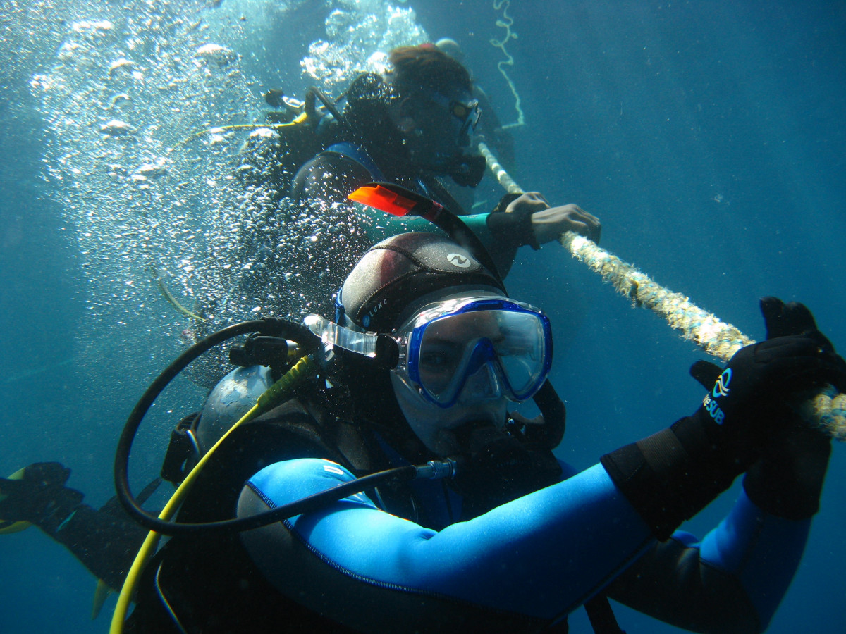 Two scuba divers holding a descent rope underwater, practicing controlled diving safety techniques
