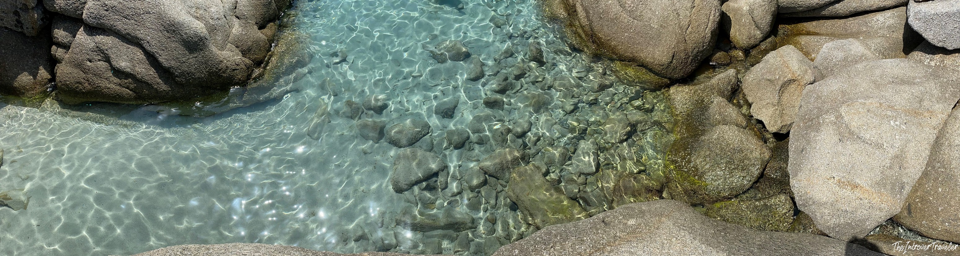 Crystal-clear shallow water between granite boulders at a south Sardinia beach cove