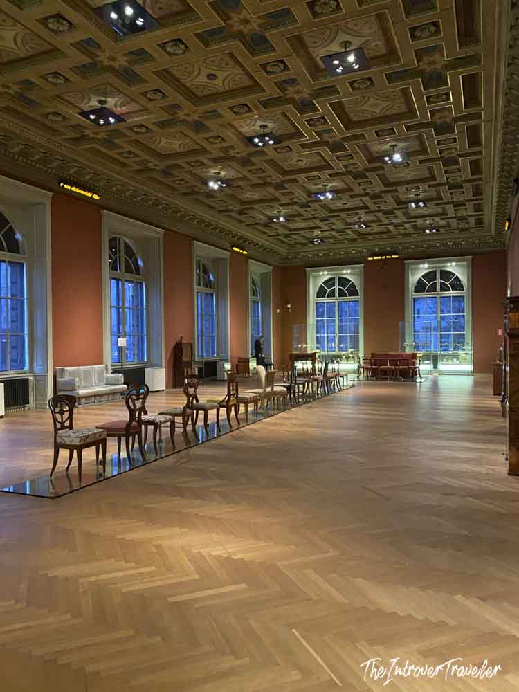 Grand hall of the MAK Museum Vienna, featuring ornate coffered ceiling, parquet floors, and antique chair displays