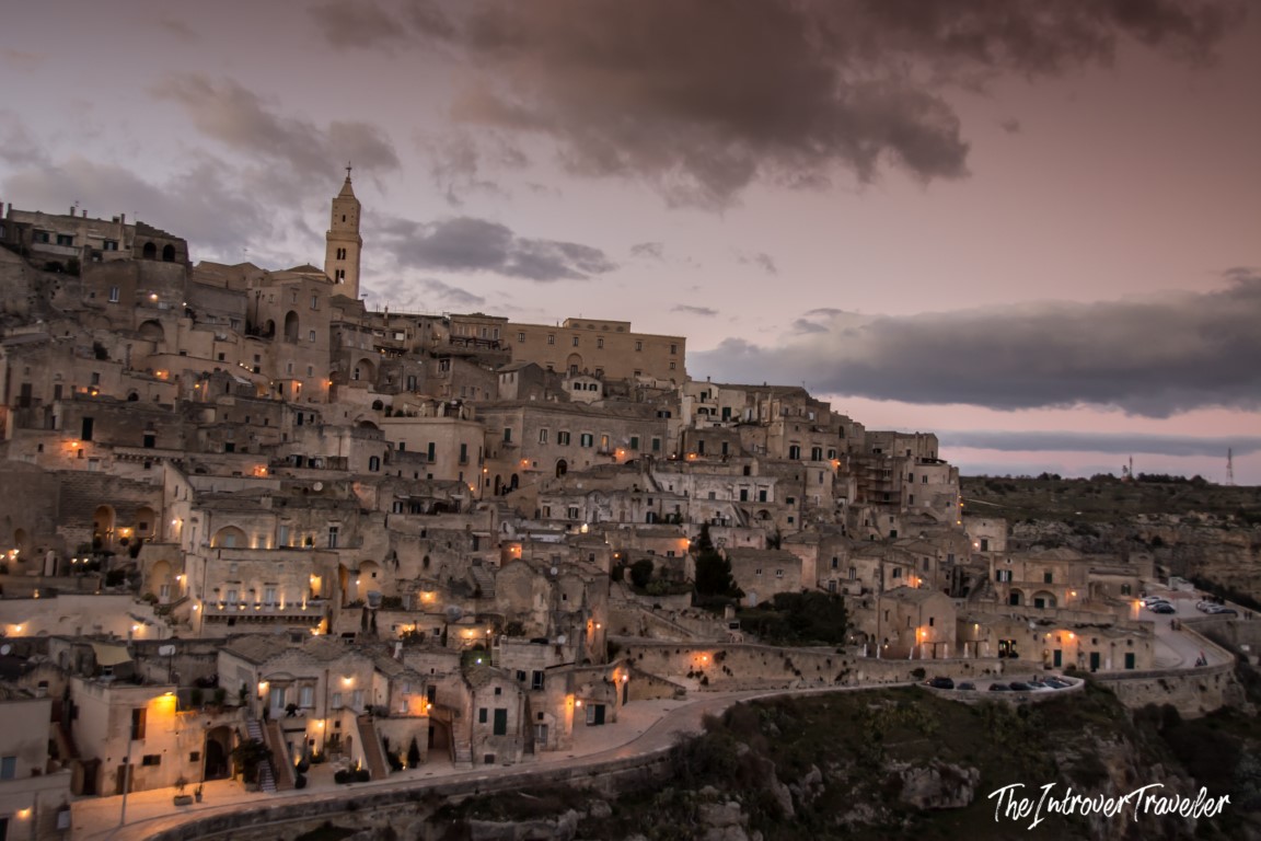 Matera Sassi cave dwellings glowing at dusk, with the Cathedral bell tower rising above