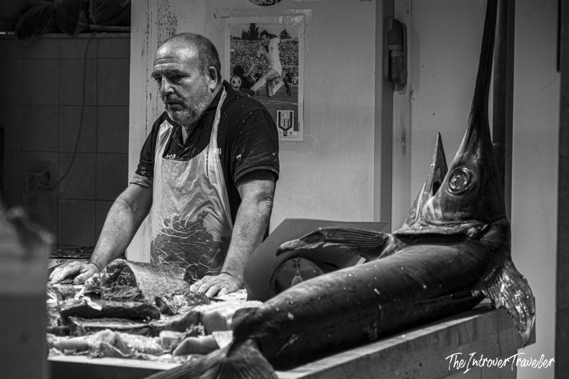 Fishmonger in apron cutting swordfish at a bustling coastal city fish market