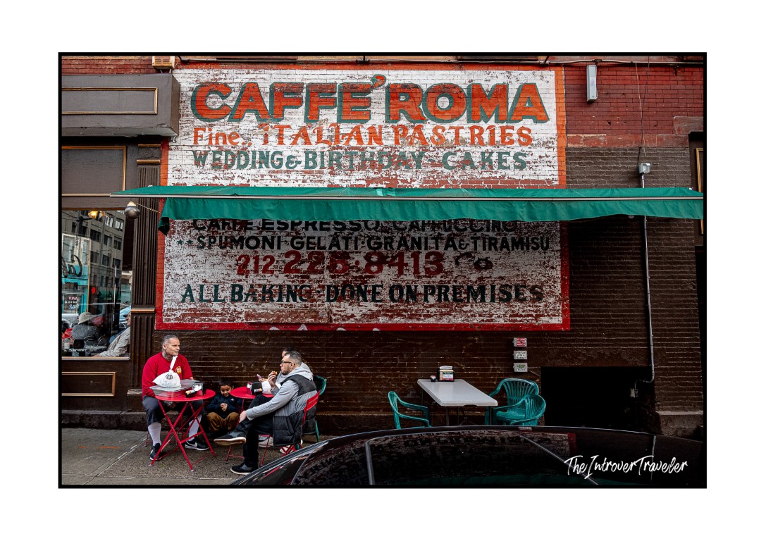 Caffe Roma in Little Italy, NYC, with locals seated at outdoor tables beneath the vintage painted facade