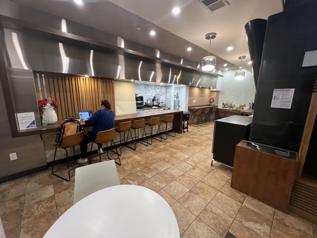 Interior of VIP One Lounge JFK with counter seating, bar stools, and a traveler working on a laptop
