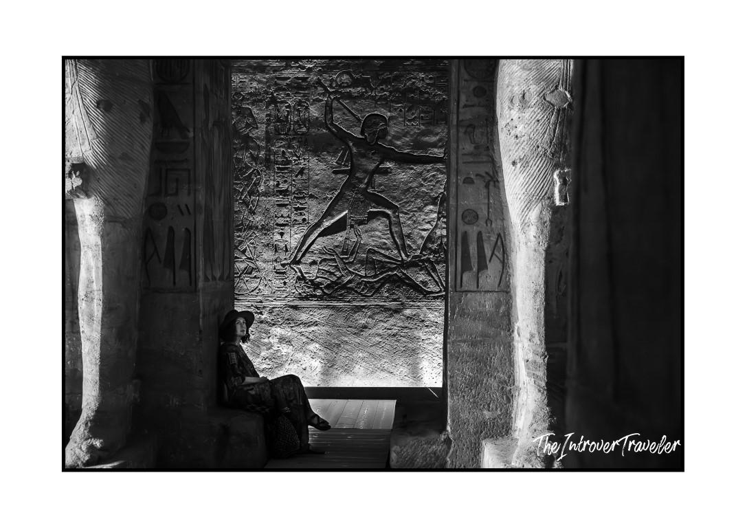 Woman sitting beside ancient Egyptian relief carvings and hieroglyphics inside a temple corridor, Egypt