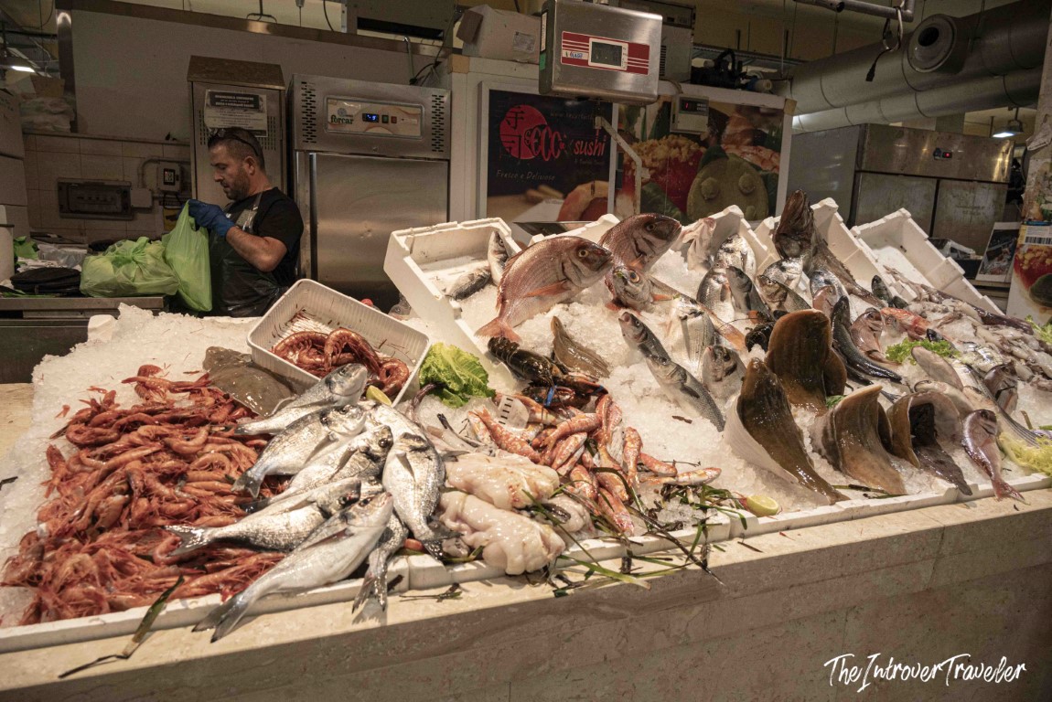 Fresh seafood display on ice at a coastal city fish market, with prawns, whole fish, and a vendor working behind the counter
