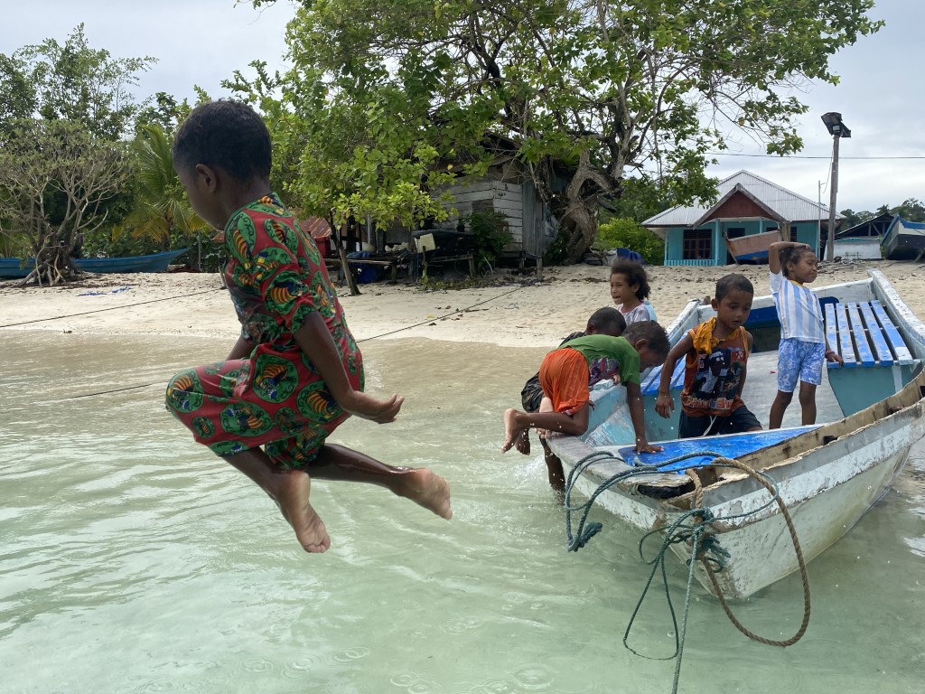 Local children playing and jumping off a fishing boat on a Raja Ampat village beach