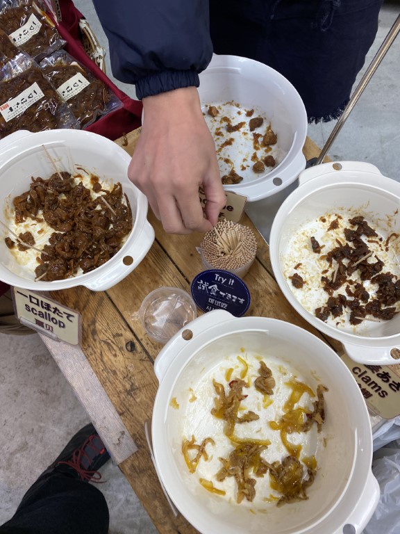 Free seafood samples at Tsukiji market, featuring scallop and clams toppings on rice