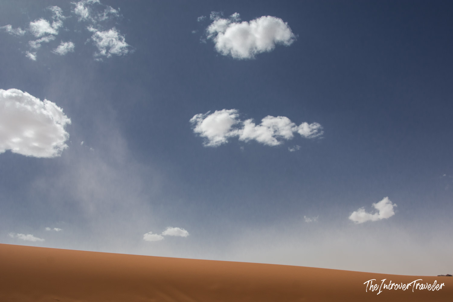 Wadi Rum desert sand dune ridge under a deep blue sky with scattered white clouds, Jordan