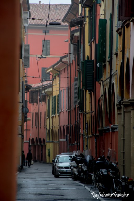 Narrow Bologna street lined with terracotta and yellow porticoed buildings, the city famous for tortellini
