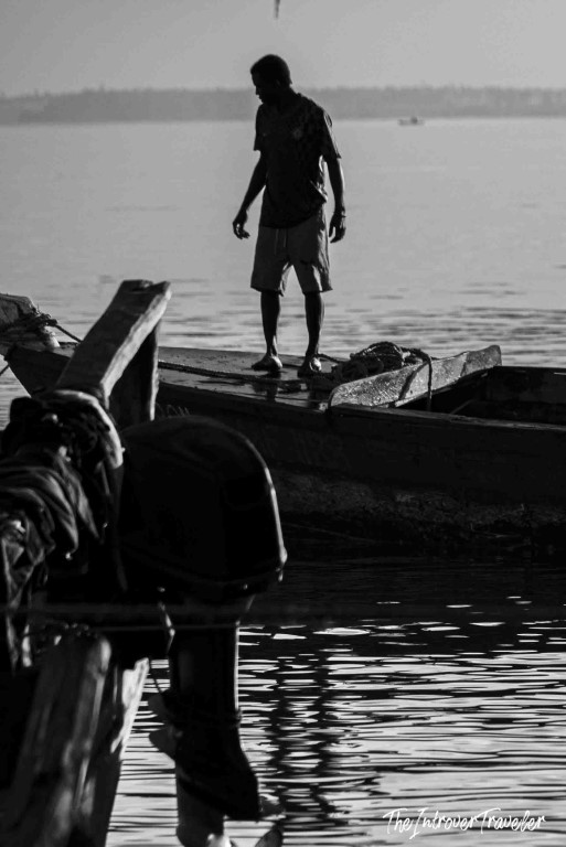 Silhouetted fisherman standing on a wooden boat at a coastal fish market harbor