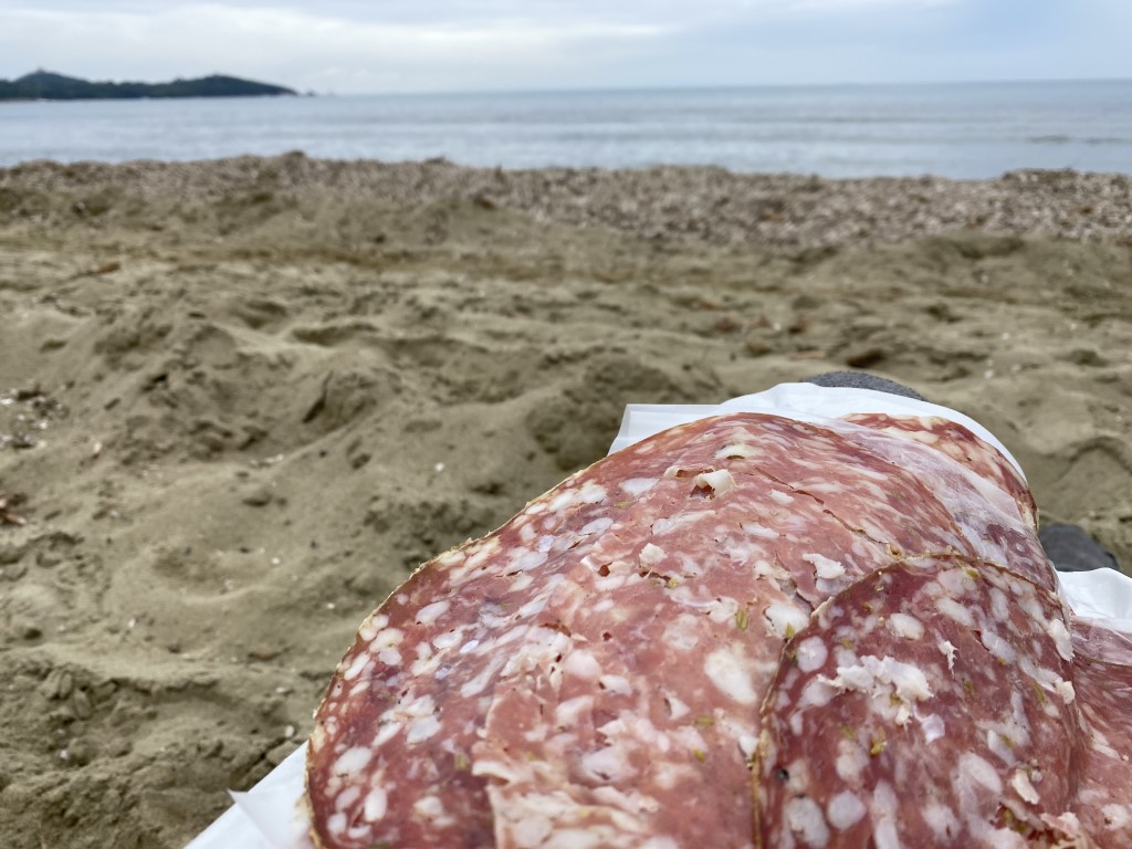 Sliced finocchiona salami on deli paper enjoyed as a beach snack along the Tuscan coast