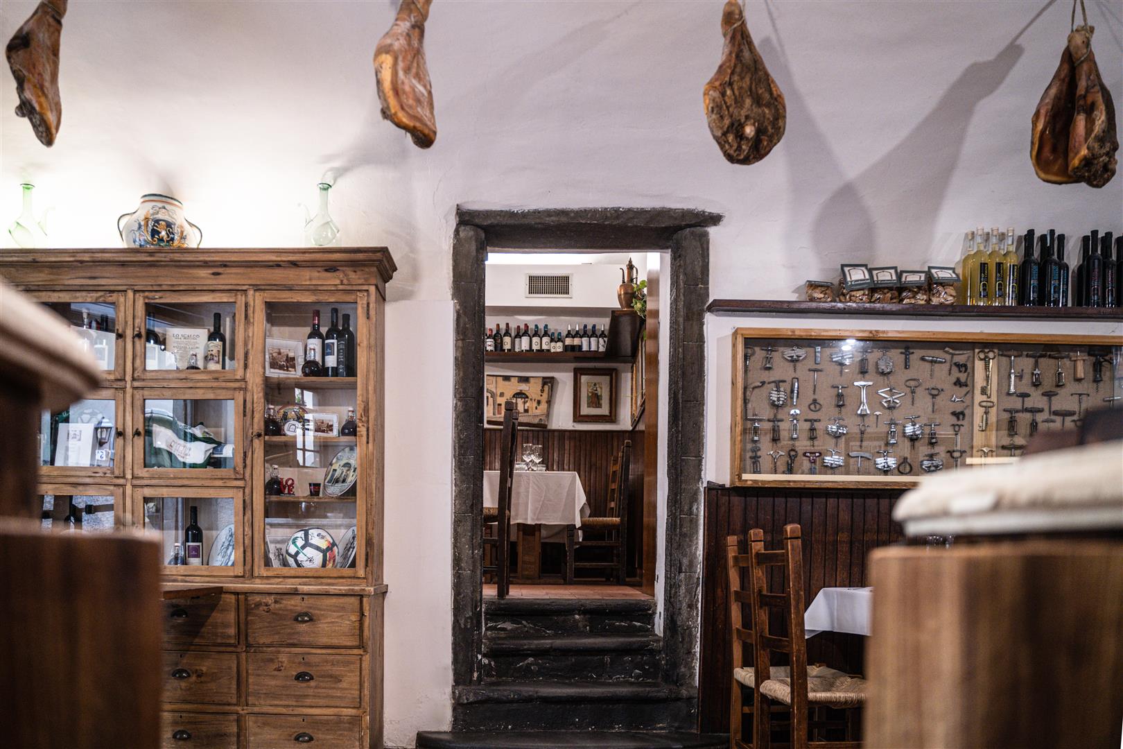 Interior of Trattoria Il Latini Florence, with hanging prosciutto legs, wine cabinet, and corkscrew display