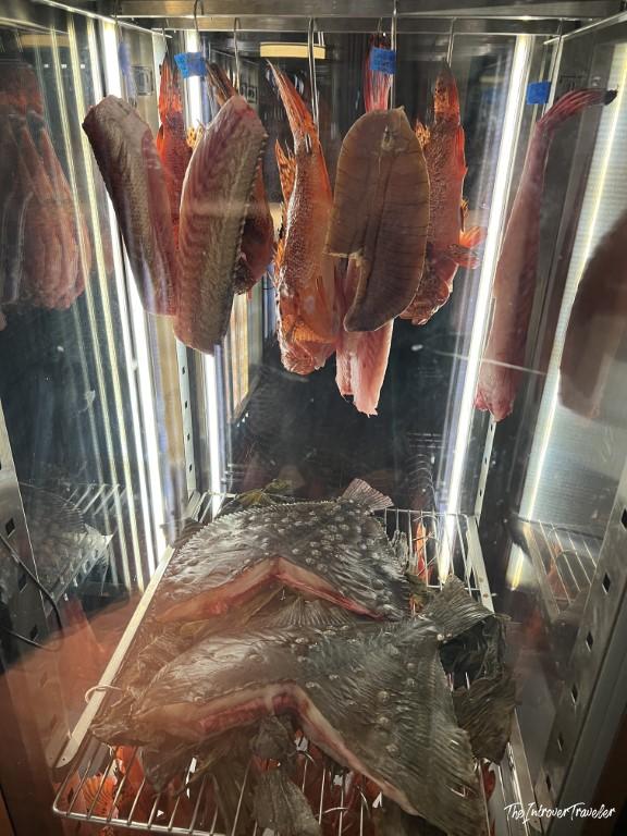 Fresh whole fish aging in a display cabinet at a Rimini seafood restaurant, with red fish hanging and flatfish on rack