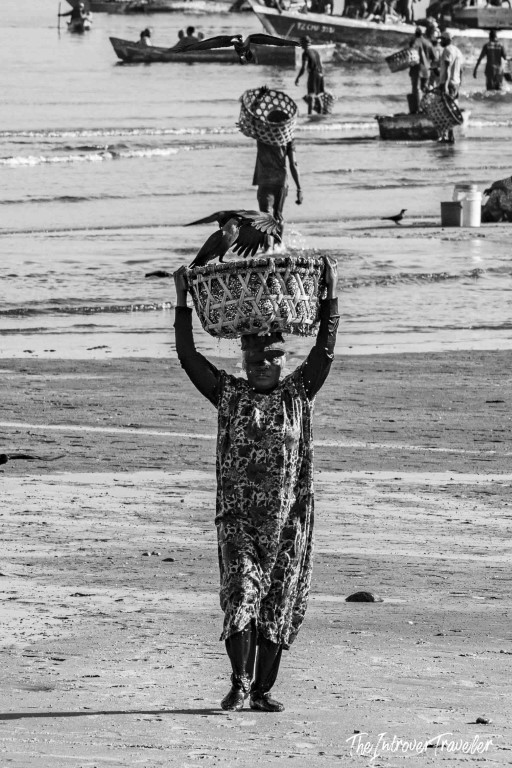 Woman carrying a woven fish basket on her head at a busy coastal fish market beach