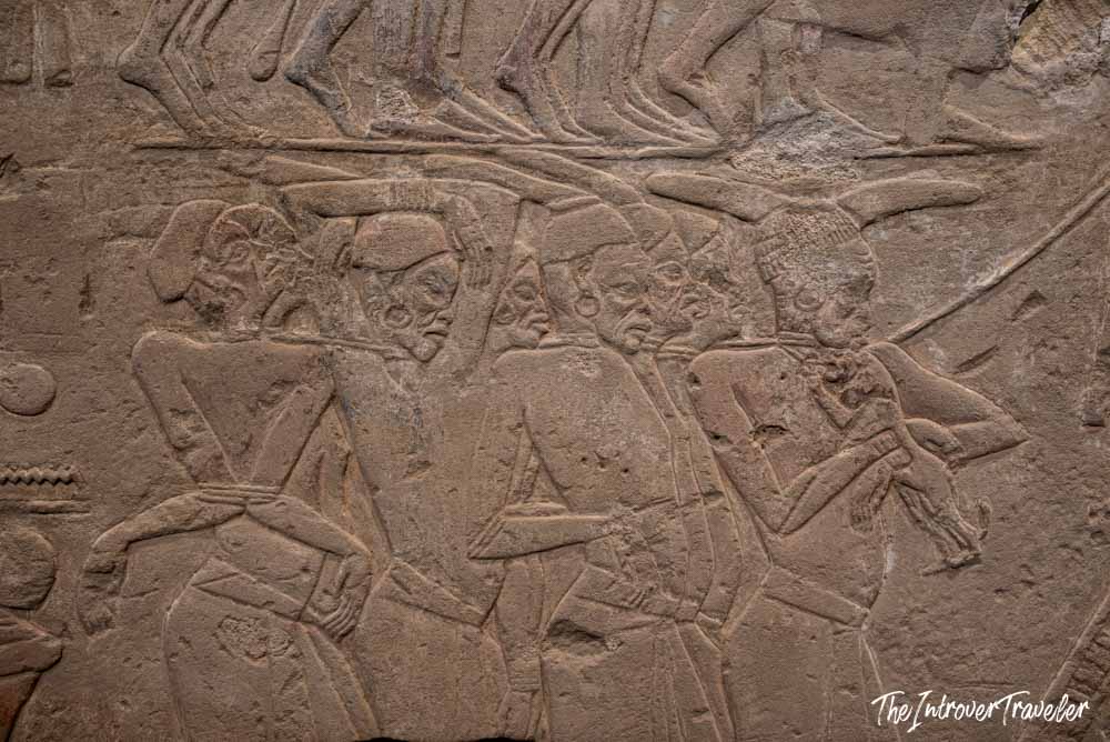 Ancient Egyptian stone relief at the Grand Egyptian Museum showing bound prisoners in detailed carved procession