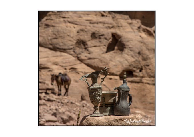 Traditional Bedouin coffee pots displayed on a rock in Petra, with sandstone cliffs and a camel behind