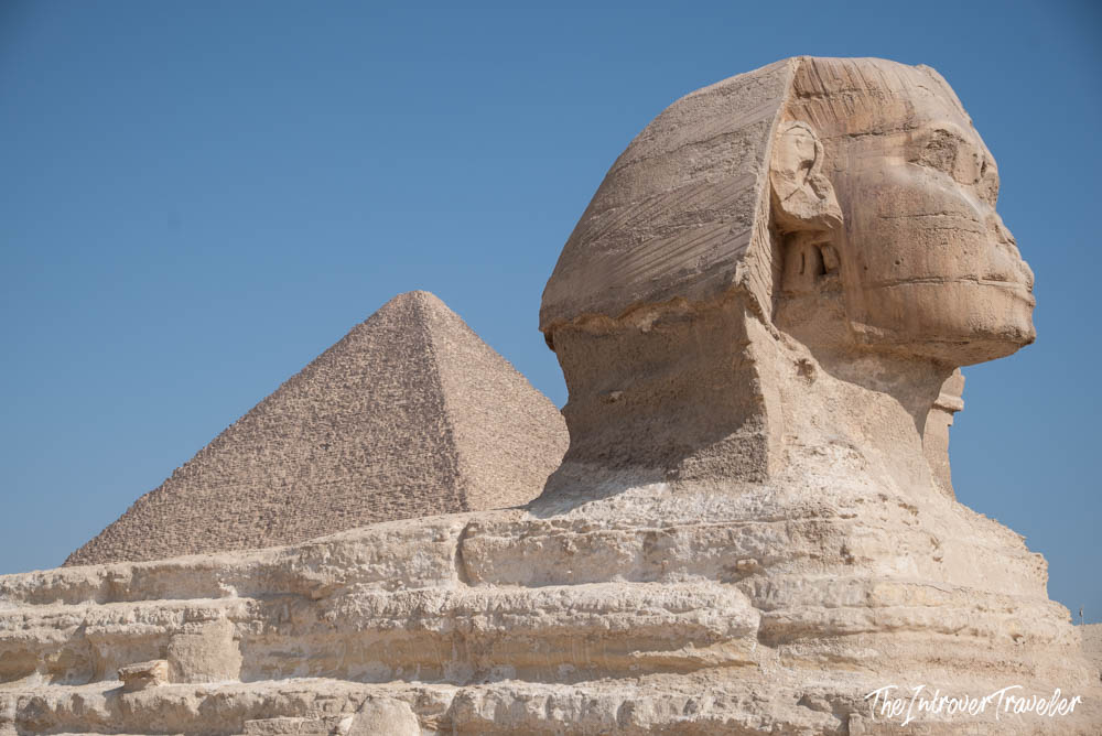 Great Sphinx of Giza in profile, with a pyramid of Giza rising behind it under a clear blue sky