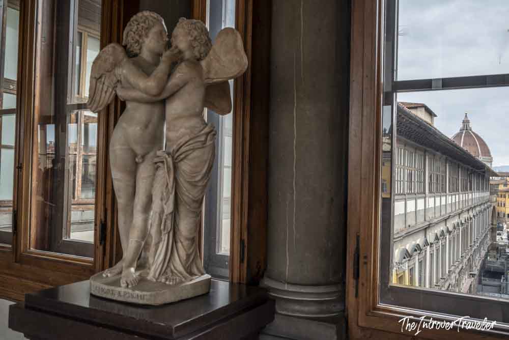 Cupid and Psyche marble sculpture in the Uffizi Gallery corridor, with Florence Duomo visible behind