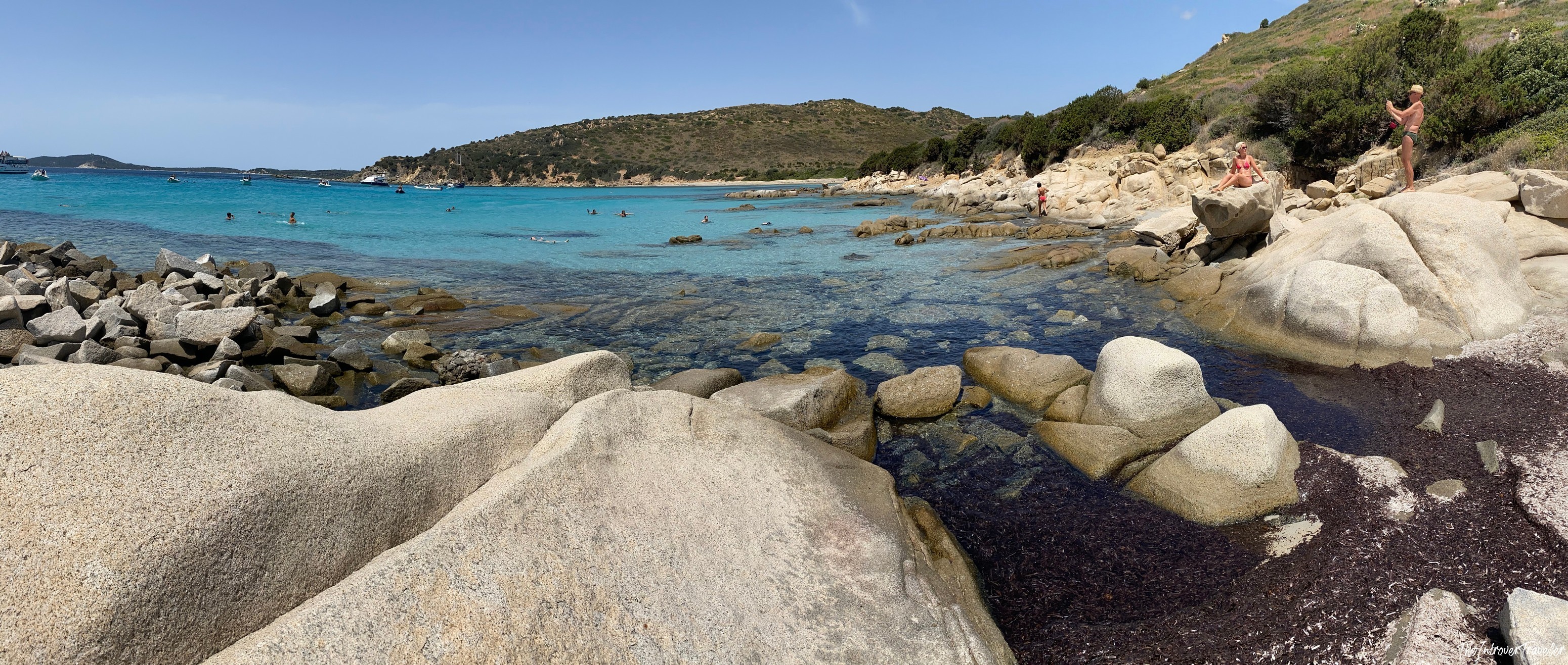 Granite boulders and turquoise water at a rocky cove on south Sardinia's coast, with swimmers and anchored boats