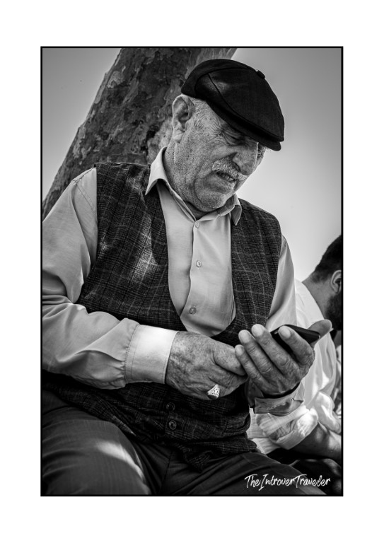 Elderly Turkish man in flat cap and waistcoat checking his phone, Istanbul street portrait