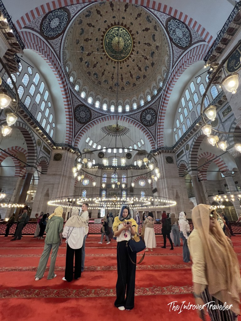 Inside the Süleymaniye Mosque, Istanbul, with ornate domed ceiling, chandeliers, and red carpeted prayer hall