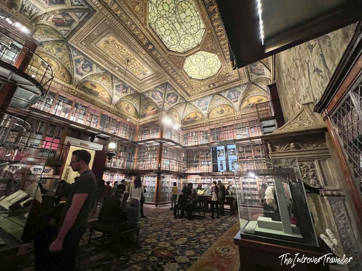 Interior of the Morgan Library East Room, with painted vaulted ceilings, stained glass skylight, and three tiers of rare books