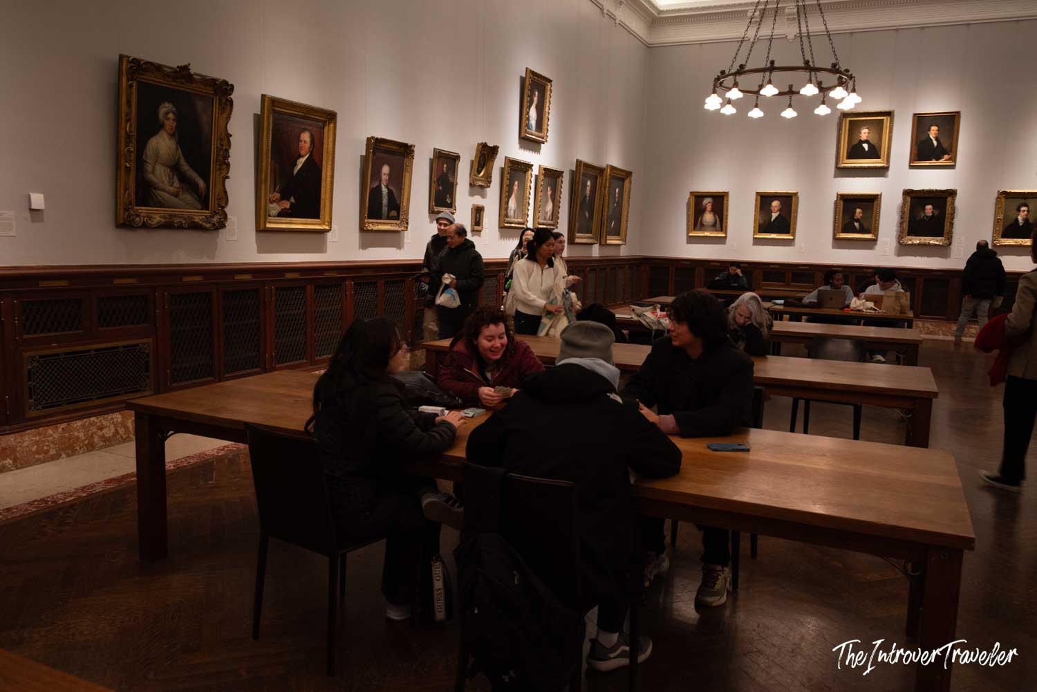 Visitors seated at wooden tables inside the New York Public Library portrait gallery room