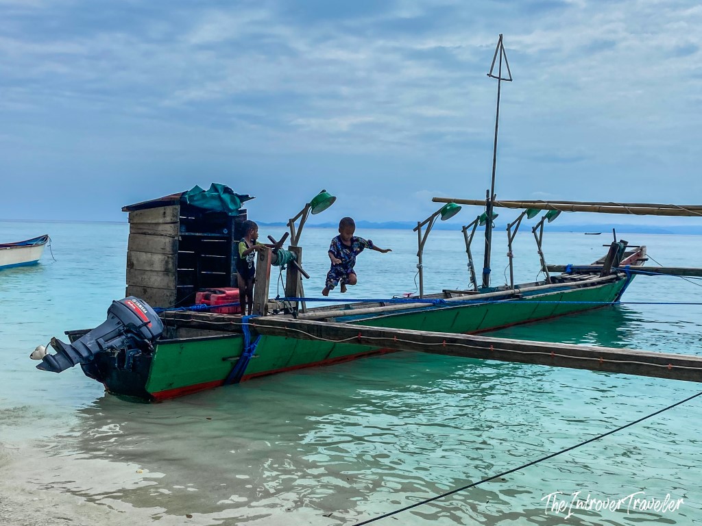 Children playing on a traditional wooden fishing boat in the turquoise waters of Raja Ampat, Indonesia