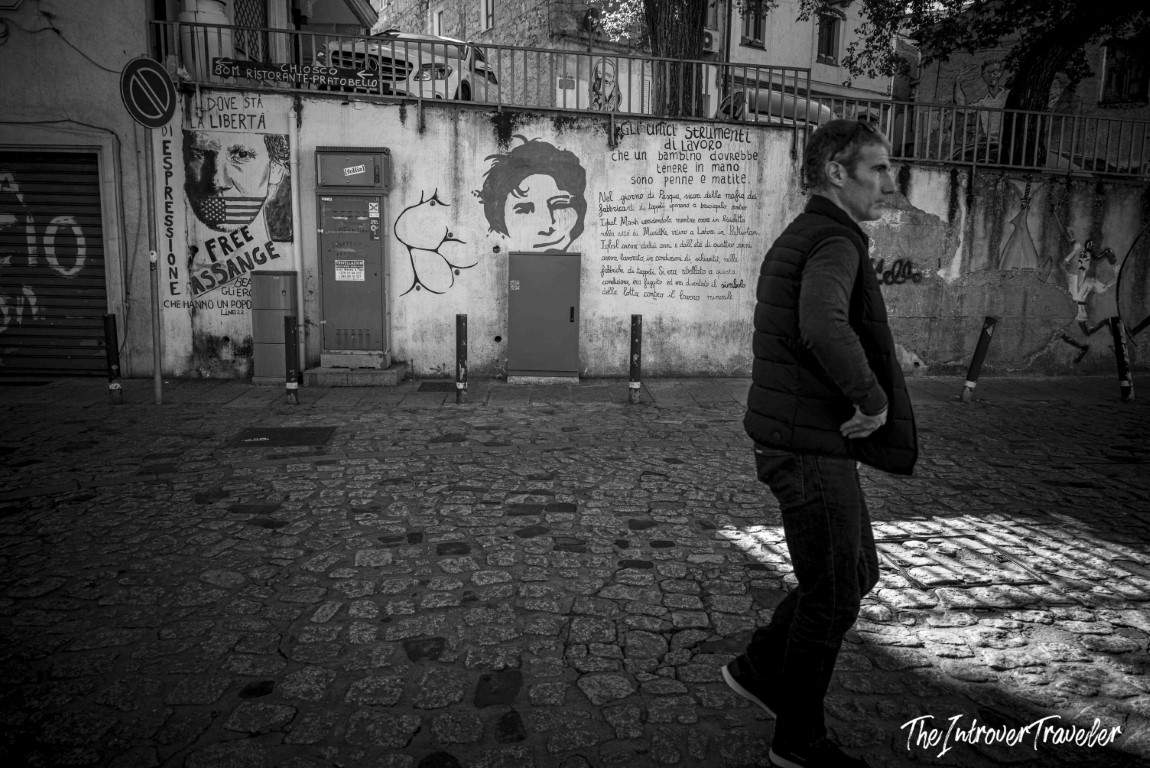 Man walking past political murals in Orgosolo, Sardinia, featuring Free Assange and child labor Italian texts