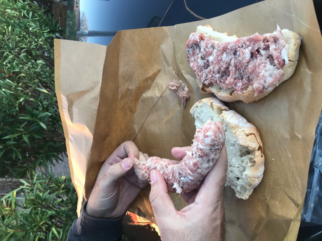 Hands spreading finocchiona salami on saltless Tuscan bread, a classic Tuscan cuisine pairing