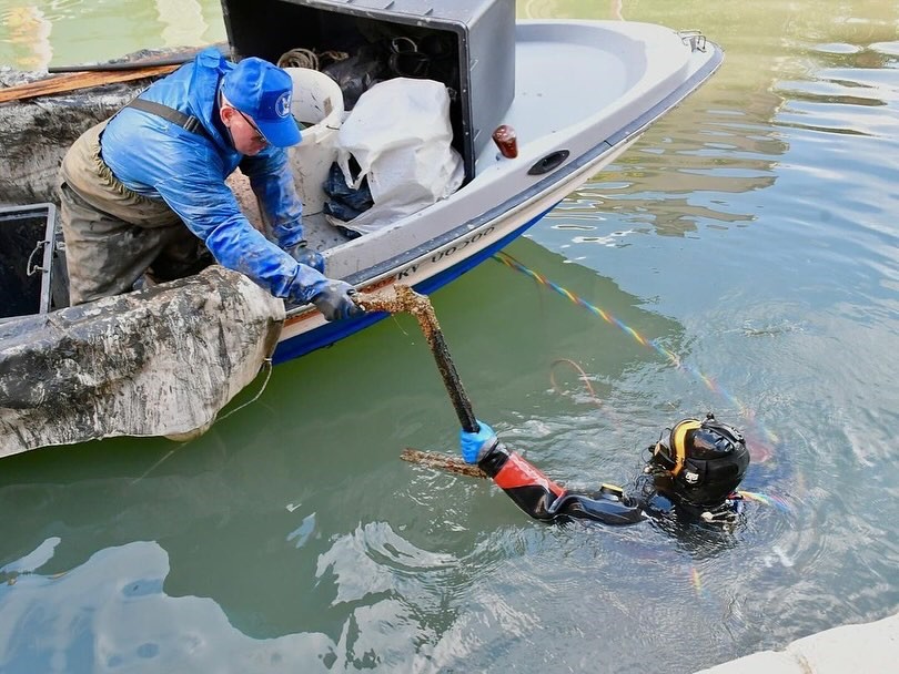 Diver and boat crew retrieving debris from a Venice canal during an underwater cleanup operation